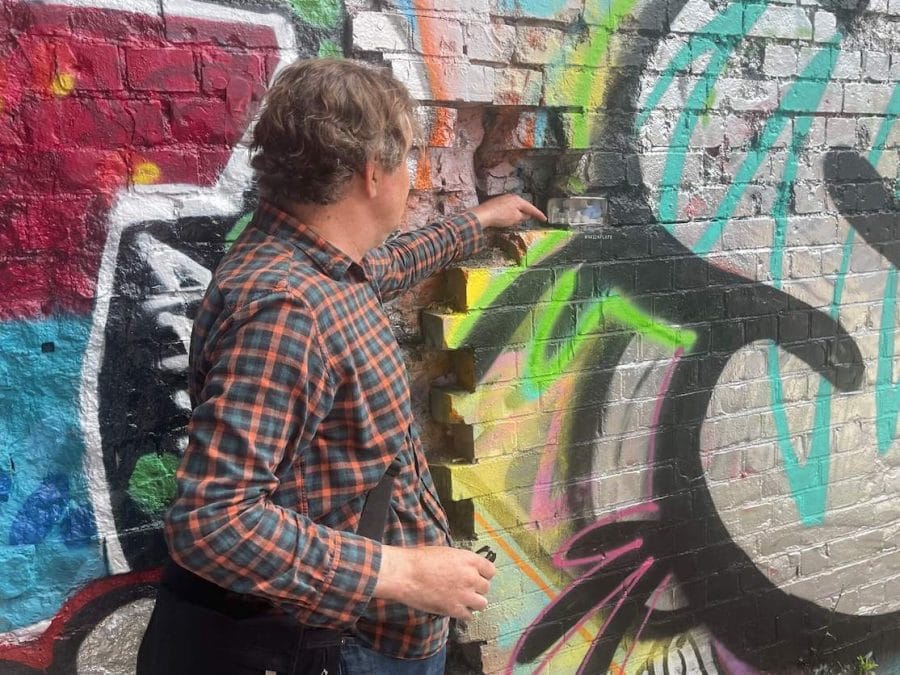 Shoreditch Street Art: Best Streets & Murals 2023 + Map 17 A guide showing a handcrafted miniature replacing a missing brick on a wall in