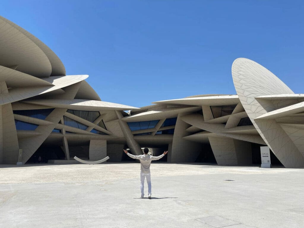 Um homem com os braços abertos em frente ao Museu Nacional do Catar