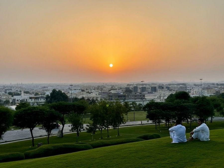Two guys wearing tradional costumes seating on the grass and watching the sunset from Katara Hills, Doha