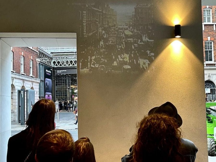A tour guide using a hand-held projection showing a picture of London in the 19th century on the wall