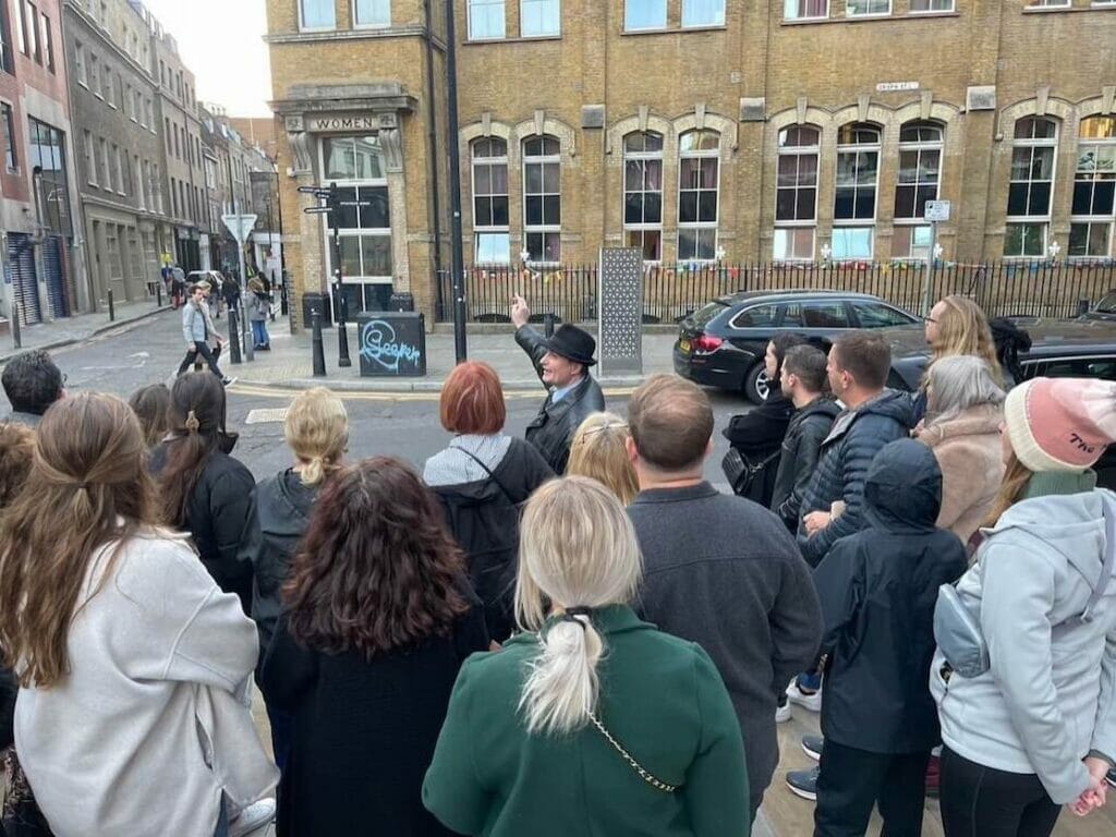 Um guia com um grupo de turistas apontando para um prédio onde foi um convento durante o passeio sobre o Jack Estripador, Londres