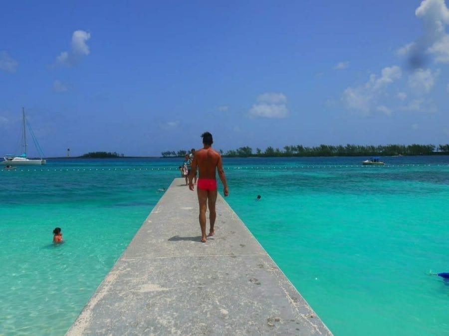 A man wearing a red speedo walking on a pier surrounded by turquoise water at Junkanoo Beach, Nassau, the Bahamas