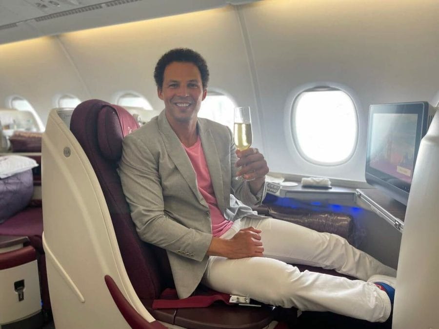 Pericles Rosa holding a glass of champagne in a Qatar Airways business class