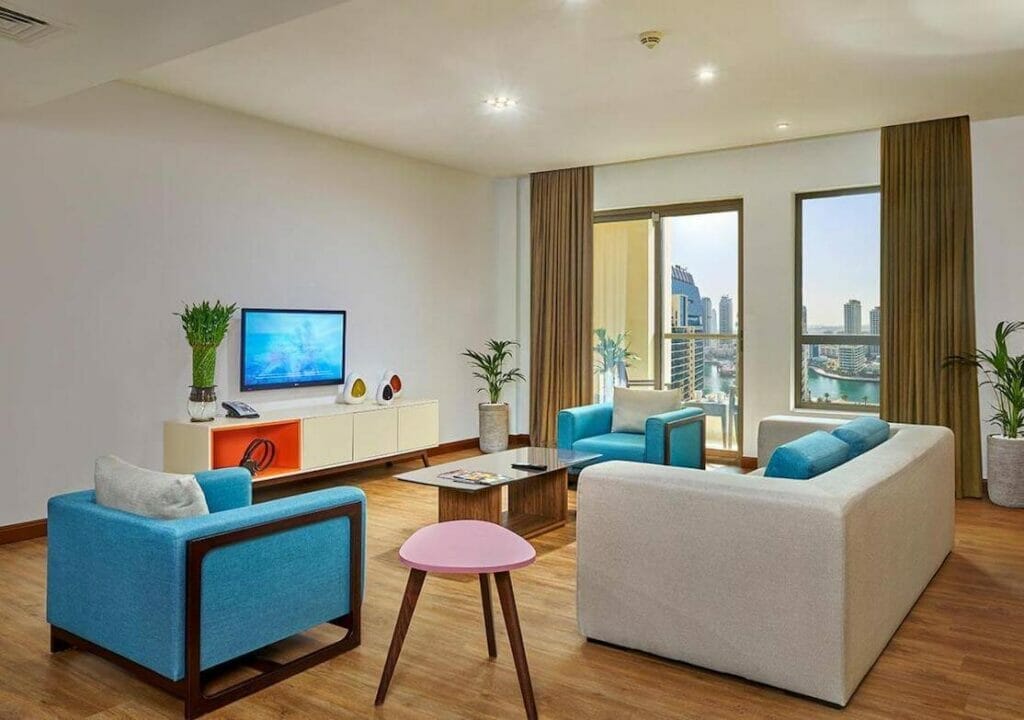 A room with a sofa, chairs, an LCD TV and city views at Ramada Hote & Suites on Jumeirah Beach Residence, Dubai