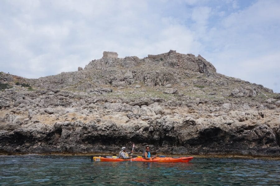 Two men kayaking in the village of Haraki with the Castle of Feraklos atop of a hill in the background, Rhodes, Greece